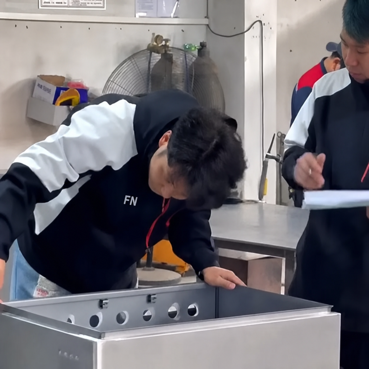 Quality inspector recording dimensional checks on a stainless steel enclosure