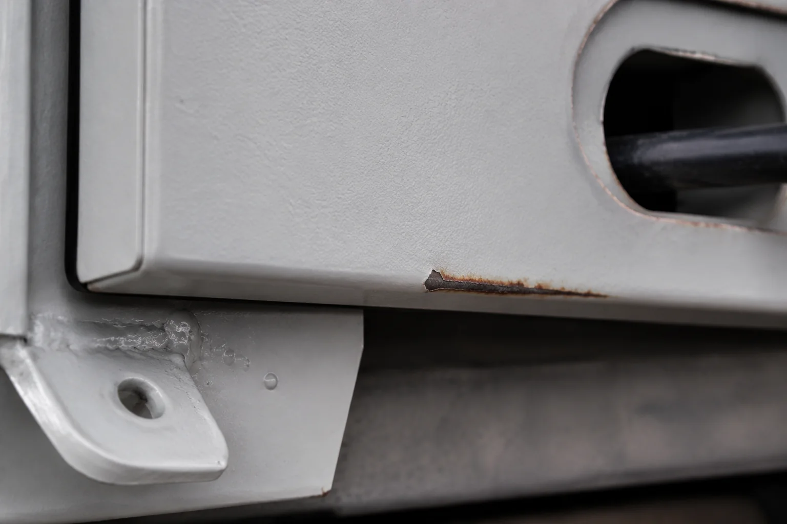 03-powder-coating-rust-creep-door-edge-weld Rust creeping beneath powder coating from a chipped enclosure door edge near a weld